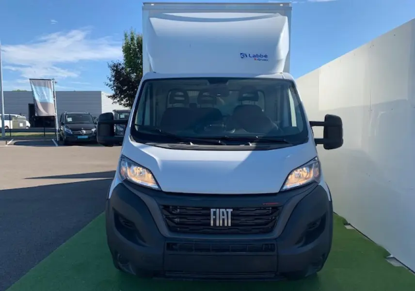 Vue frontale d'un fourgon blanc Fiat Ducato Business 2022 avec hayon et calandre noire visible au soleil.