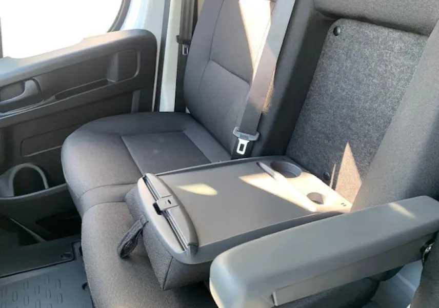 Intérieur du Fiat Ducato Fourgon blanc, vue rapprochée sur la banquette passager biplace avec tablette rabattable et accoudoir.