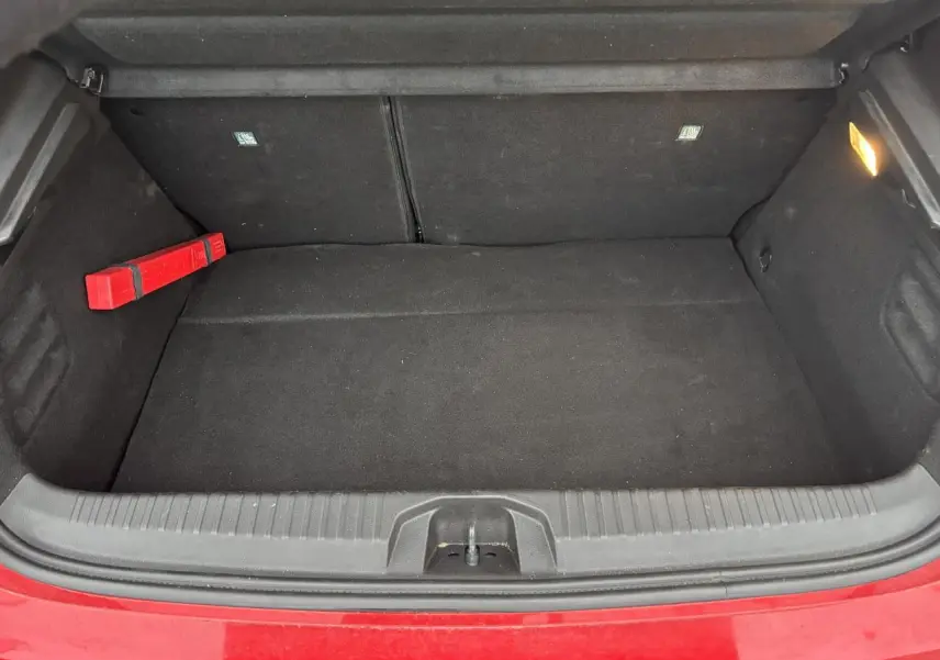 Coffre ouvert vu de face d'une Renault Clio rouge flamme, intérieur noir avec triangle de signalisation à gauche.