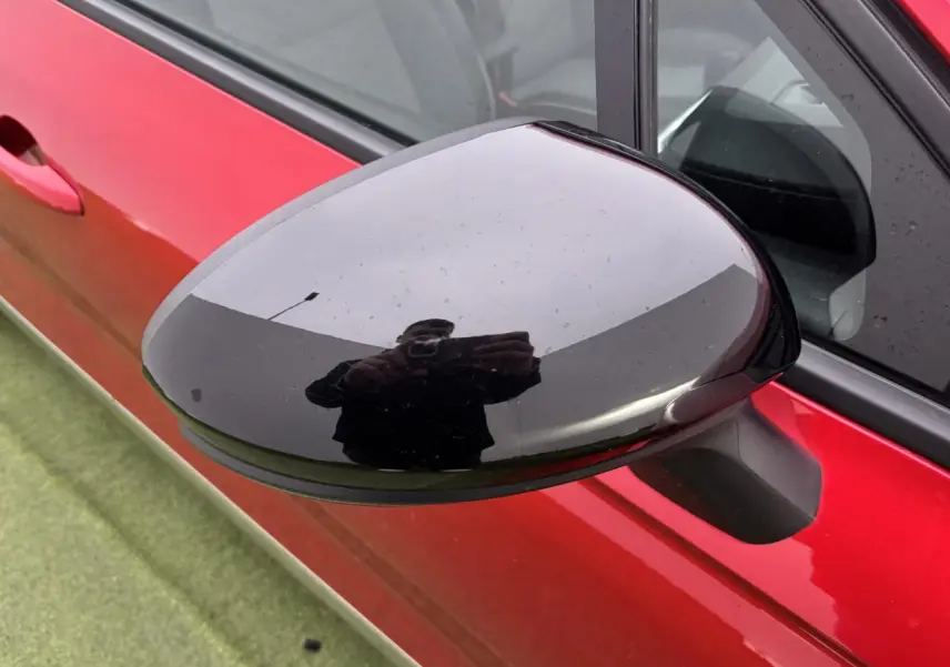 Rétroviseur extérieur noir brillant côté gauche sur porte rouge flamme d'une Renault Clio V hybride 2025.