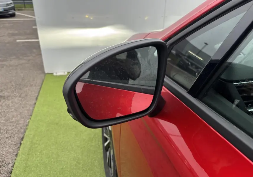 Rétroviseur côté gauche d’une Renault Clio rouge flamme métal, avec partie avant et vitre visible.