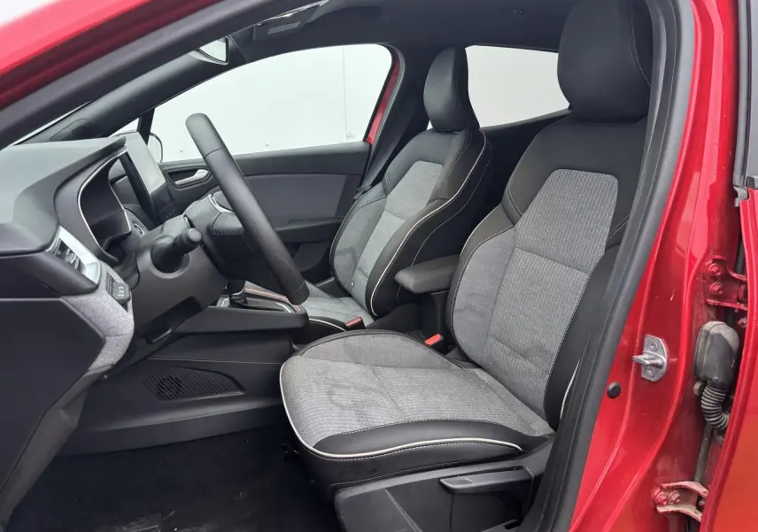 Vue intérieure côté conducteur de la Renault Clio rouge flamme, sièges bi-matière gris et noir avec accoudoir coulissant.