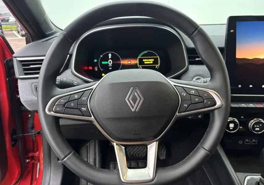 Vue rapprochée du volant multifonction noir et du tableau de bord numérique de la Renault Clio V rouge flamme 2025.