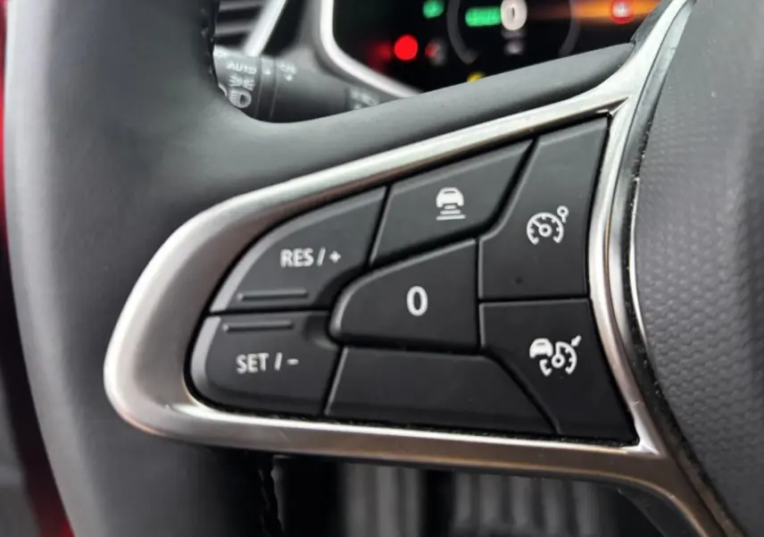 Gros plan sur les commandes au volant à gauche de la Renault Clio V rouge flamme, boutons de régulateur de vitesse et assistance.