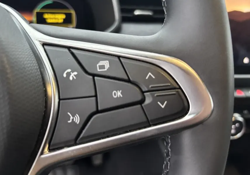 Gros plan sur les commandes multifonctions noires à gauche du volant de la Renault Clio rouge flamme 2025.