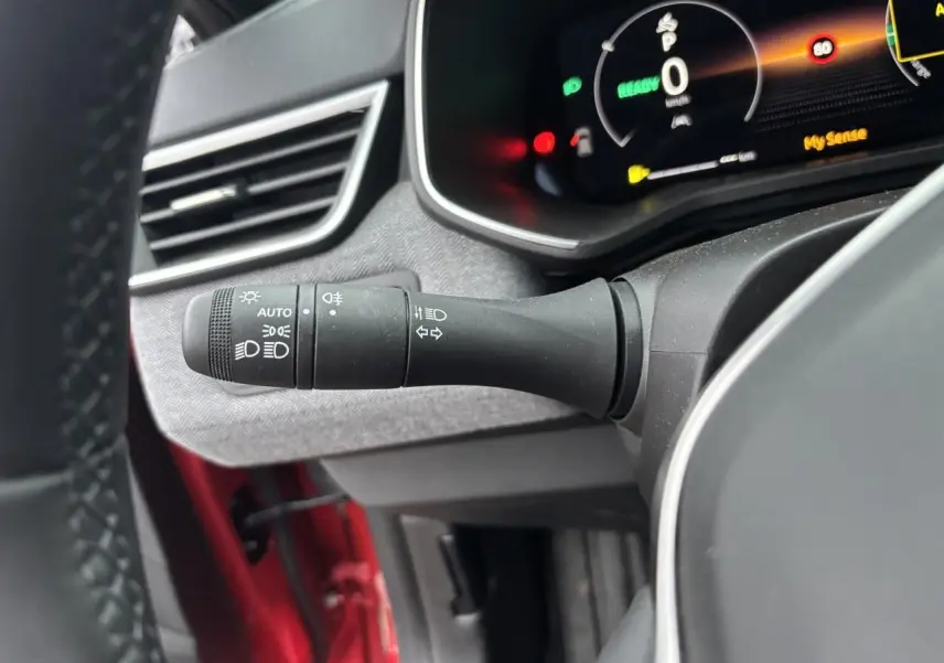 Gros plan sur la commande des phares et clignotants côté gauche du volant, intérieur gris et rouge flamme visible.