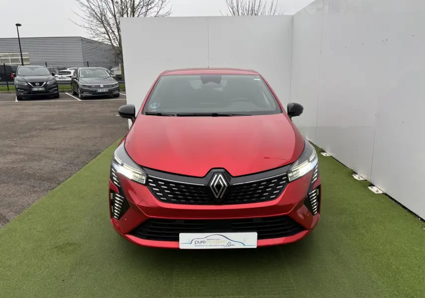 Renault Clio V hybride rouge flamme vue de face, avec calandre noire et feux LED allumés.