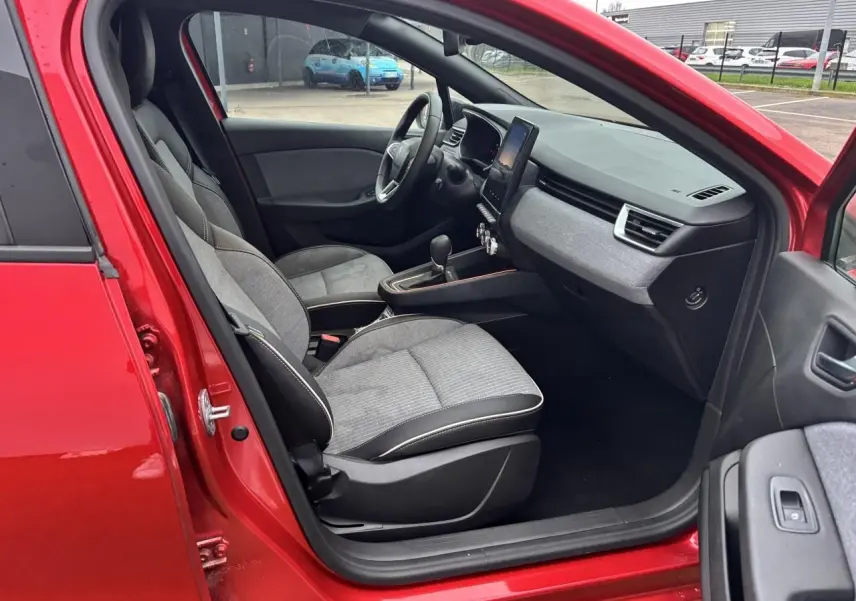 Vue intérieure côté gauche de la Renault Clio V rouge flamme, montrant sièges gris et tableau de bord avec écran tactile.