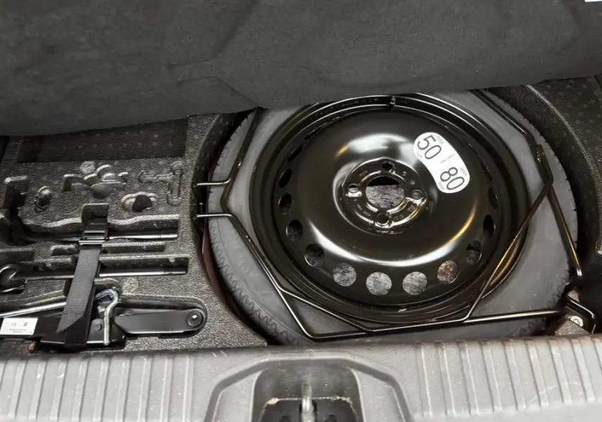 Vue rapprochée de la roue de secours noire et des outils de bord dans le coffre d'une Renault Clio rouge flamme.