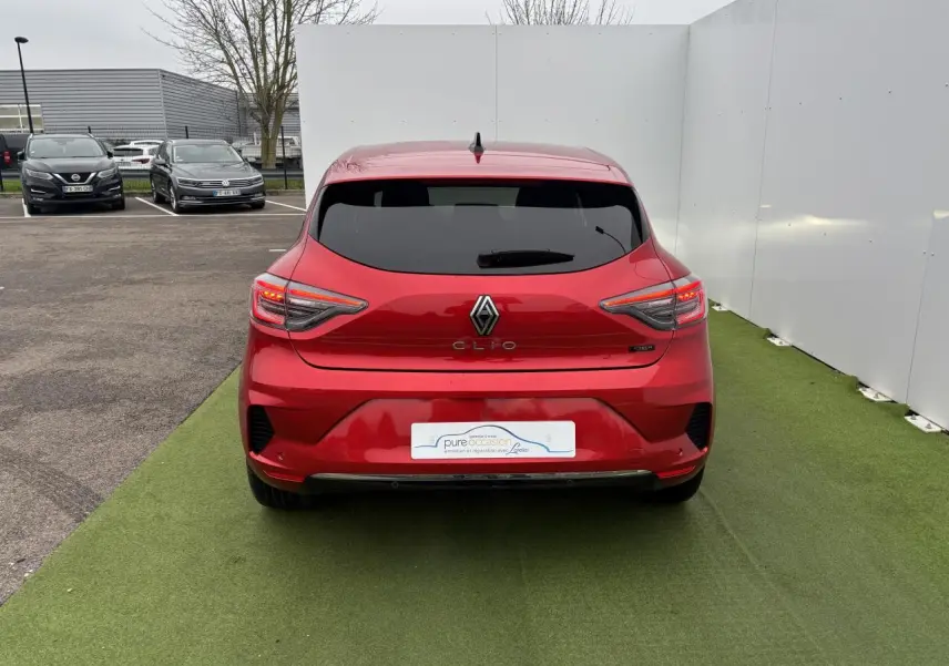 Vue arrière d'une Renault Clio 2025 rouge flamme métal avec feux arrière LED en forme de C et vitre arrière surteintée.
