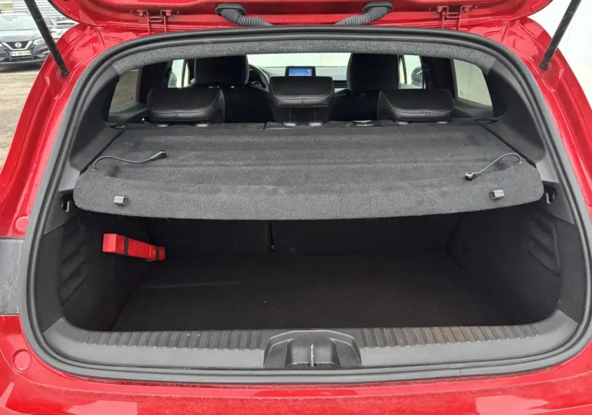 Coffre ouvert vu de l'arrière d'une Renault Clio V rouge flamme, avec cache-bagages en place et sièges arrière visibles.