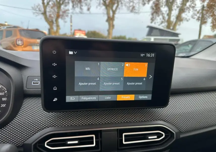 Écran tactile central du tableau de bord de la Dacia Sandero blanc, avec menu radio affiché en extérieur.