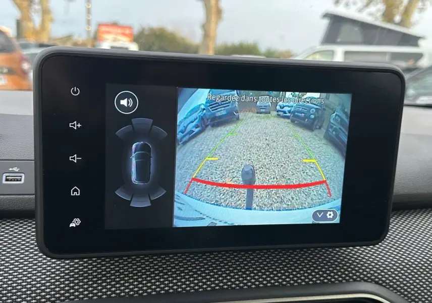 Écran intérieur montrant la caméra de recul active d'une Dacia Sandero blanche, vue depuis le poste de conduite.