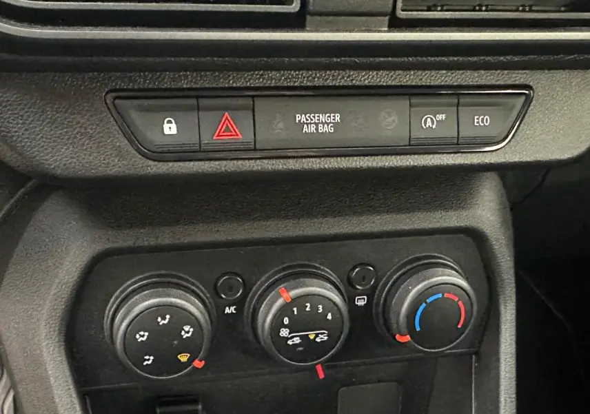 Vue rapprochée du tableau de bord de la Dacia Sandero 2024, montrant les commandes de climatisation manuelle et les boutons de sécurité.