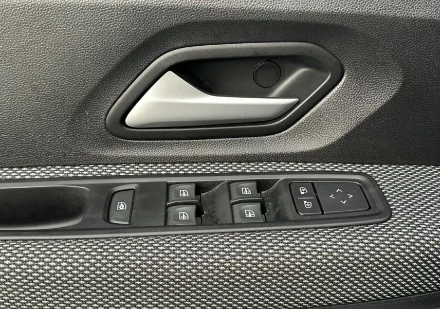 Gros plan sur la poignée intérieure et les commandes des vitres côté gauche d’une Dacia Sandero blanche, tissu gris texturé.