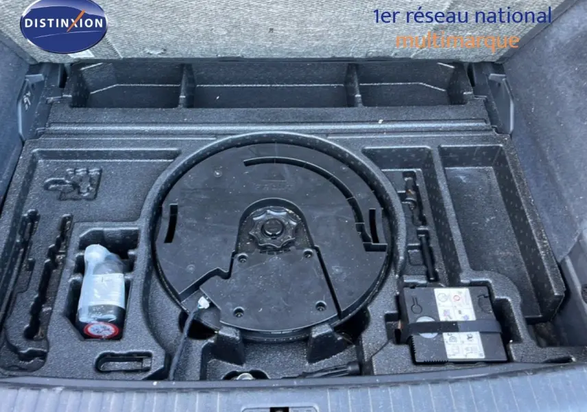Vue plongeante sur le coffre ouvert d’un Audi Q3 Sportback noir mythic, montrant le rangement pour roue de secours et outils.
