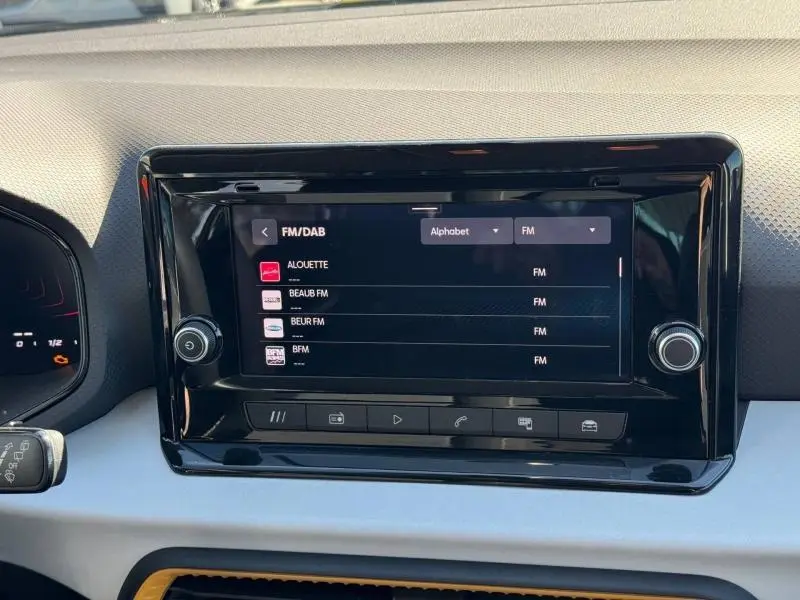 Vue rapprochée de l'écran tactile central noir brillant du tableau de bord du SEAT Arona 2025, affichant les radios FM/DAB.