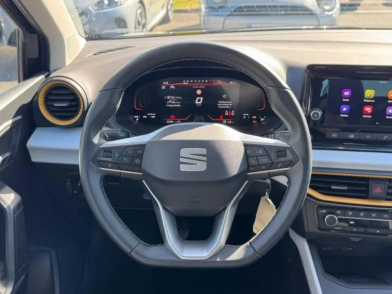 Vue intérieure centrée sur le volant multifonction de la SEAT Arona 2025 avec tableau de bord numérique et écran tactile.
