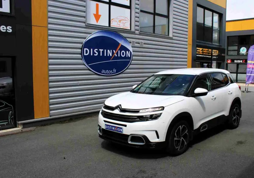 Citroën C5 Aircross blanc en 3/4 avant droit, avec jantes noires et toit contrasté noir, stationné devant un mur métallique.