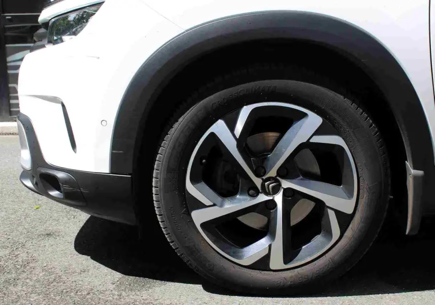 Gros plan sur la roue avant gauche et partie du pare-chocs d’un Citroën C5 Aircross blanc avec jante alliage bicolore.