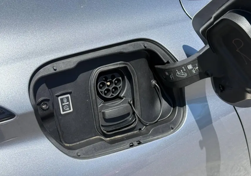 Prise de recharge électrique ouverte sur le côté gauche d’une Peugeot e-308 gris Artense métallisé.