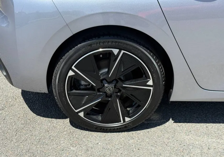 Gros plan sur la roue arrière droite d’une Peugeot e-308 gris Artense avec jante alu noire et argentée au design moderne.