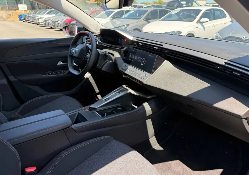 Vue intérieure côté conducteur de la Peugeot e-308 2025, tableau de bord moderne avec écran tactile et sièges tissu gris.