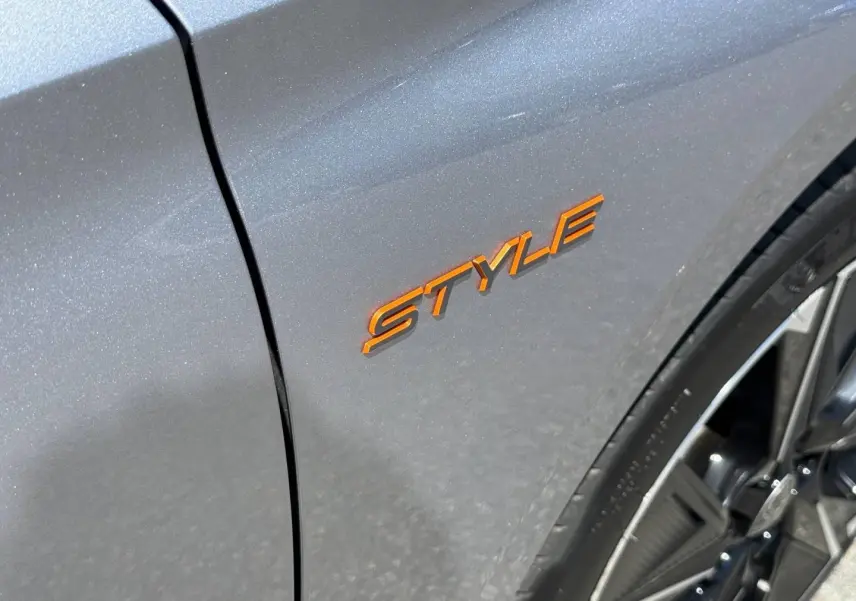 Gros plan sur l’aile avant droite gris Artense avec logo Style orange et jante alu visible.