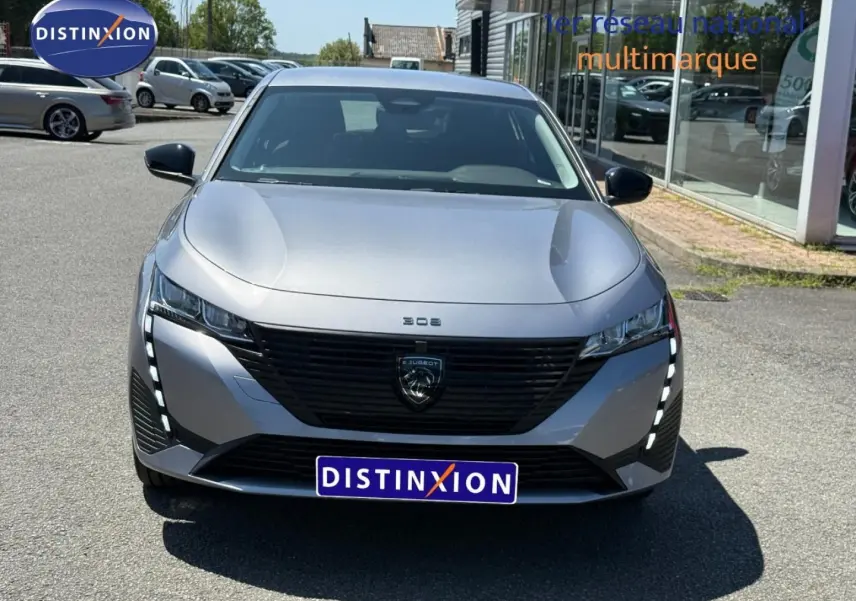 Vue avant d'une Peugeot 308 e-308 gris Artense avec calandre noire et feux LED verticaux allumés.