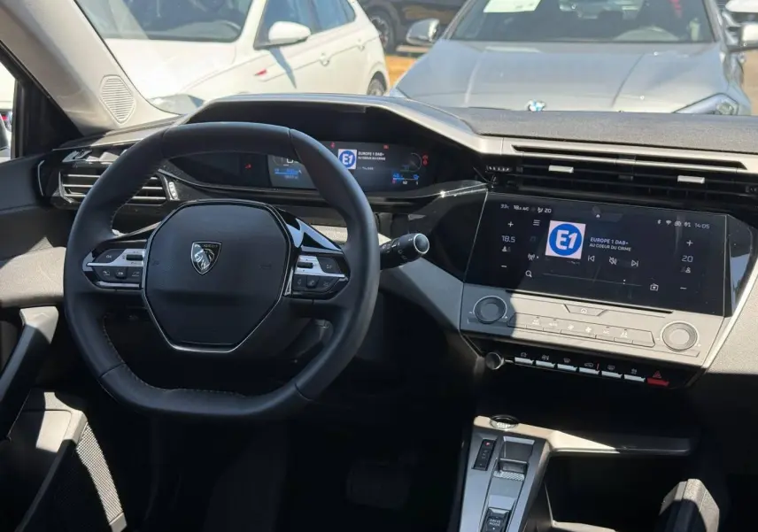 Vue intérieure du poste de conduite de la Peugeot e-308 gris Artense, avec volant multifonction et écran tactile central.