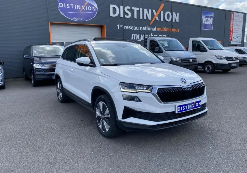 Vue 3/4 avant d'un Skoda Karoq blanc moon métallisé avec jantes alliage, stationné devant un concessionnaire Distinxion.