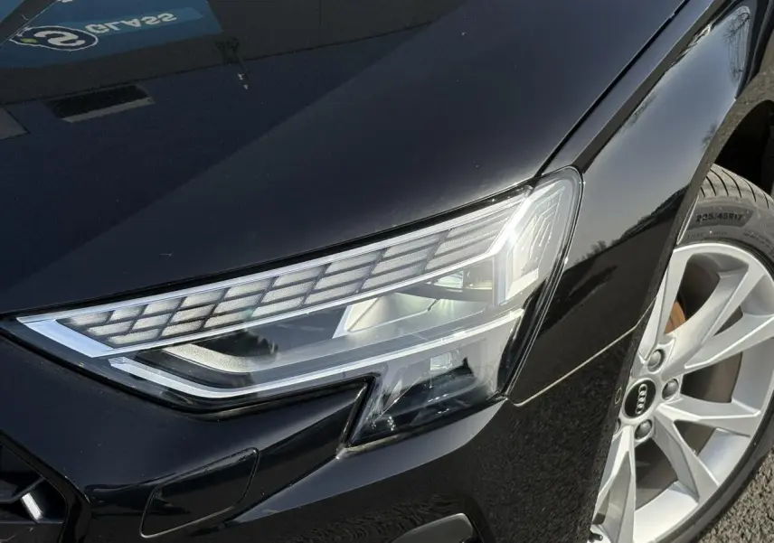 Gros plan sur le phare avant droit et la jante alliage 17 pouces de l'Audi A3 Berline noir Mythe 2024.