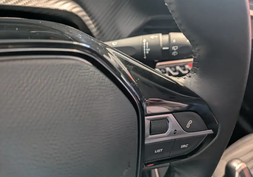 Gros plan sur le côté droit du volant cuir noir de la Peugeot 208 2024 avec commandes intégrées.