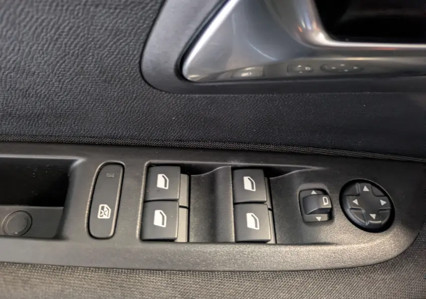 Gros plan sur les commandes des vitres électriques et réglages des rétroviseurs côté conducteur d'une Peugeot 208 noir perla.
