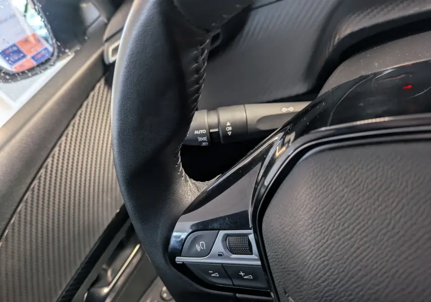 Gros plan sur le volant cuir noir de la Peugeot 208 PureTech 100 S&S BVM6 Active, avec commandes intégrées.