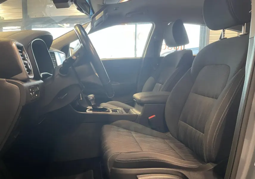 Vue intérieure côté conducteur du Kia Sportage gris clair 2021, mettant en valeur les sièges tissu noirs et l'accoudoir central.