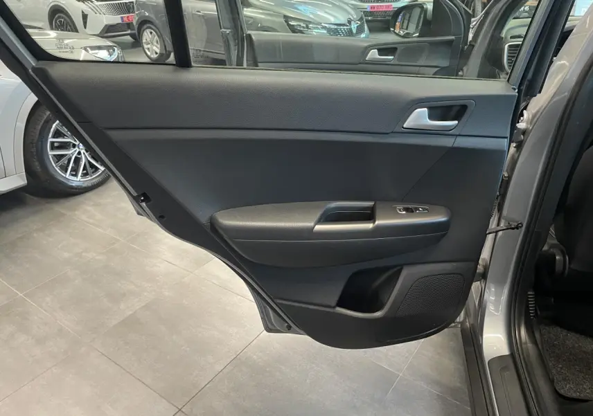 Porte arrière droite ouverte d’un KIA Sportage gris clair, montrant la garniture intérieure noire avec commandes de lève-vitres.