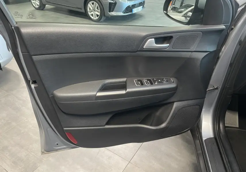 Porte avant gauche ouverte du Kia Sportage gris clair 2021, avec commandes électriques et haut-parleur intégré.