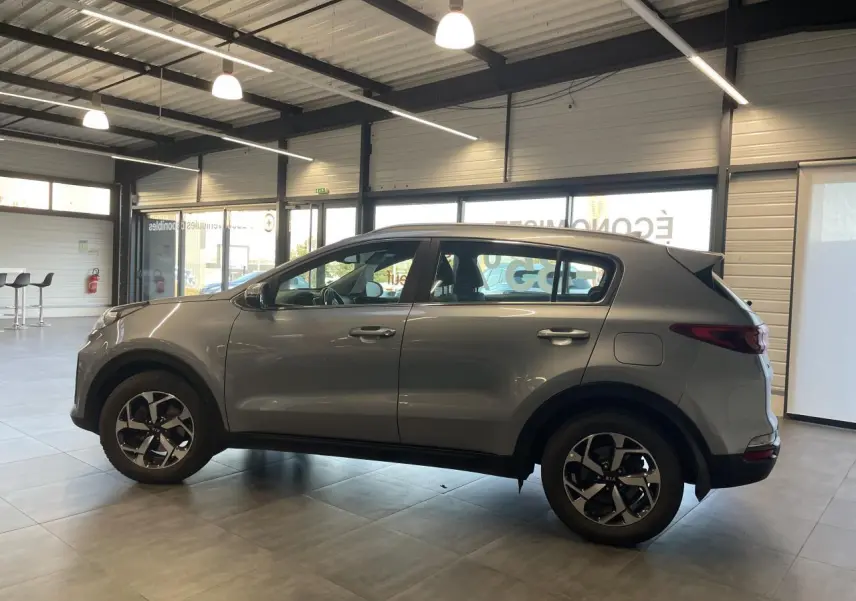 Vue de profil côté gauche d'un Kia Sportage gris clair 2021 en showroom avec jantes alliage 16 pouces.