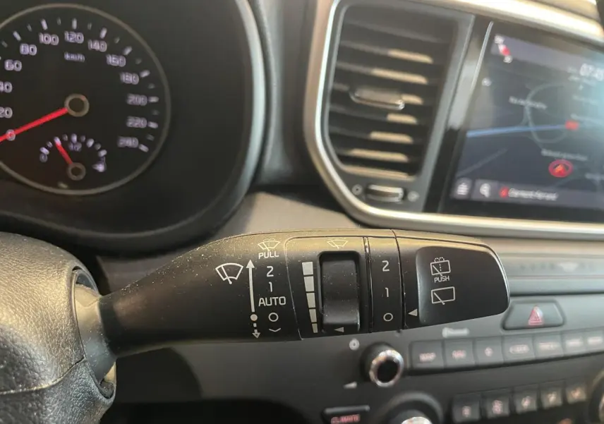 Gros plan sur la commande des essuie-glaces dans l’habitacle noir du Kia Sportage gris clair, avec écran tactile en arrière-plan.