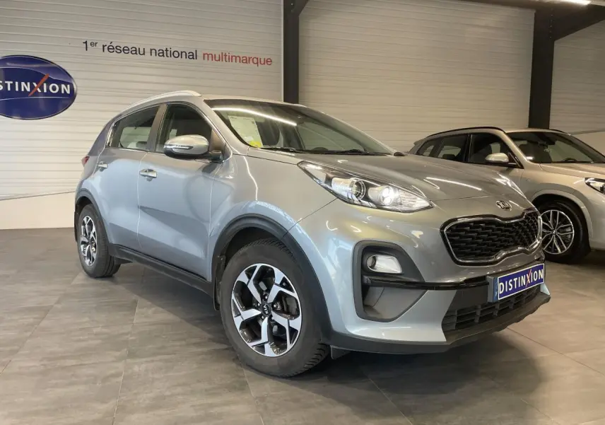 KIA Sportage gris clair en 3/4 avant droit, avec jantes alliage 16 pouces et calandre noir mat.