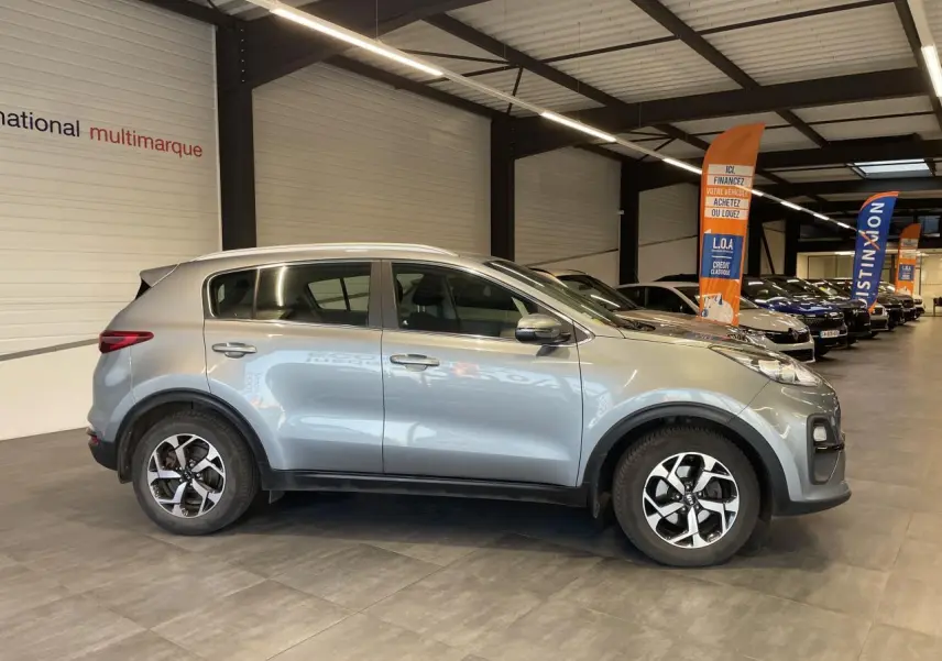 KIA Sportage gris clair vu de profil côté gauche, avec jantes alliage 16 pouces et poignées couleur carrosserie.