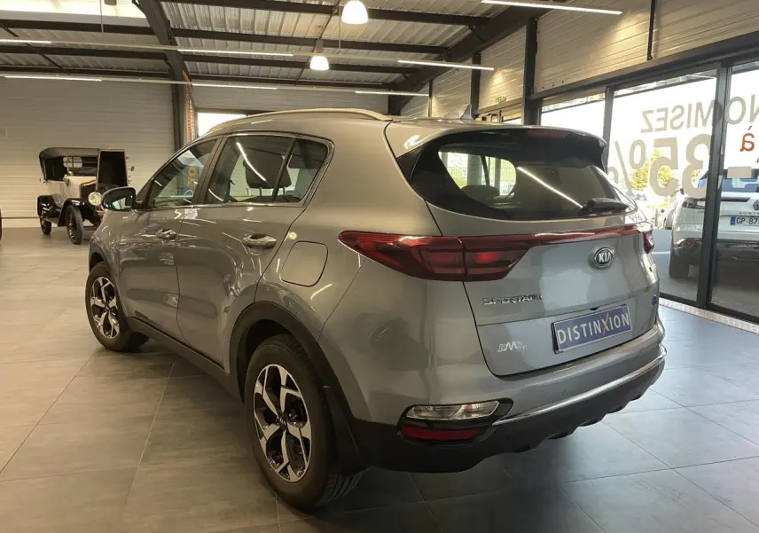 Vue 3/4 arrière droite du KIA Sportage gris clair 2021 avec jantes alliage et becquet arrière intégré.