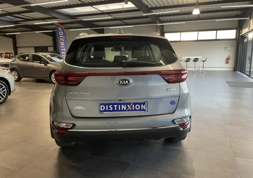Vue arrière d'un KIA Sportage gris clair en showroom, avec feux arrière reliés par une bande rouge et logo central.