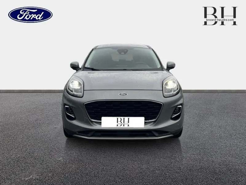 Vue avant d'un Ford Puma 2023 gris Solar métallisé avec calandre noire et phares allumés sur sol gris.