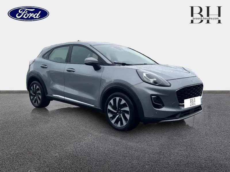 Ford Puma 2023 gris Solar métallisé en 3/4 avant droit, avec jantes alliage et calandre noire distinctive.