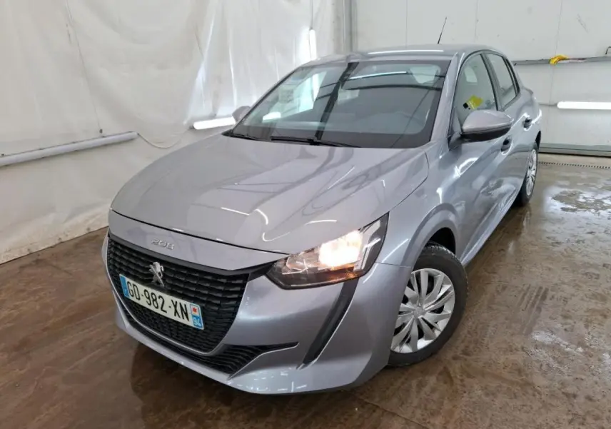 Peugeot 208 gris Artense vue 3/4 avant droit avec phares allumés dans un garage fermé.