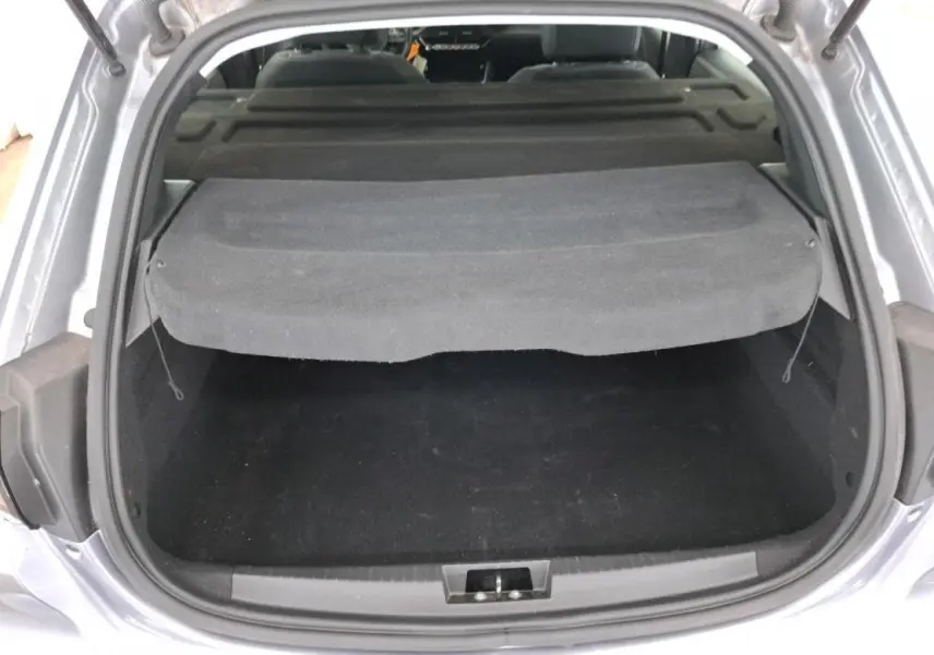 Coffre ouvert vu de l'arrière d'une Peugeot 208 gris Artense avec cache-bagages noir relevé.