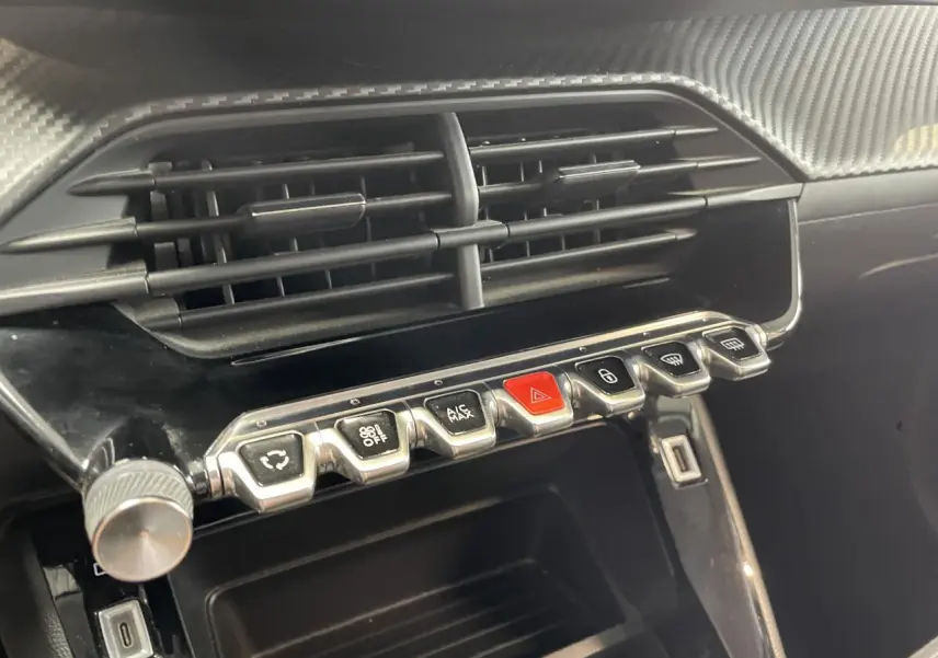 Gros plan sur la console centrale noire brillante de la Peugeot 208 avec rangements et boutons de commande alignés.