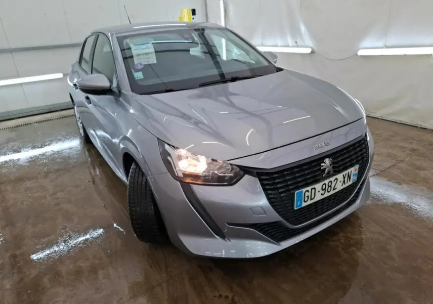 Peugeot 208 gris Artense vue 3/4 avant gauche avec calandre noire et feu avant allumé dans un garage.